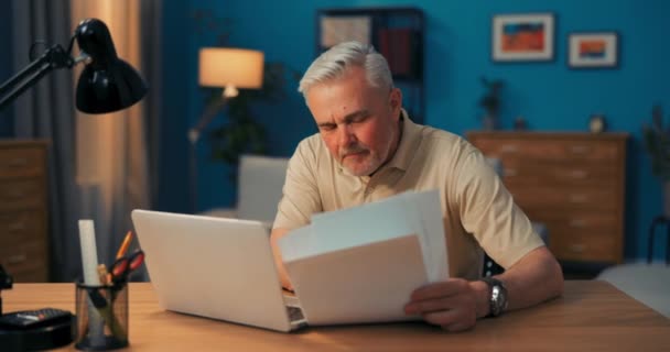 Aufnahme eines älteren Geschäftsmannes, der vor einem Laptop mit Dokumenten sitzt. Mann arbeitet aus der Ferne in — Stockvideo