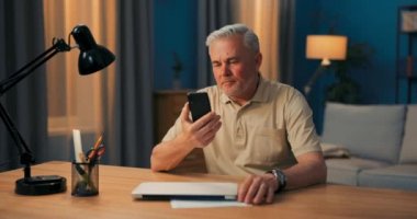 Bir iş adamı çevrimiçi konferanslar düzenler. Yaşlı bir adam telefondaki web kamerasına gülüyor. Yaşlı bir yönetici.