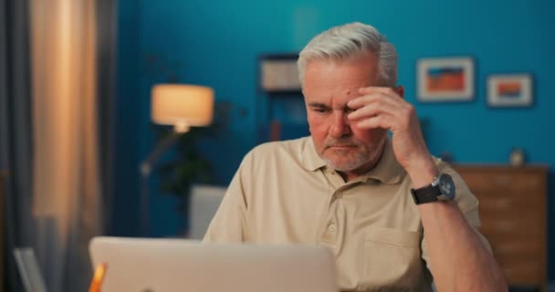 Homem idoso cansado de se sentar na frente do laptop. Sénior homens suporta cabeça com mão. — Vídeo de Stock