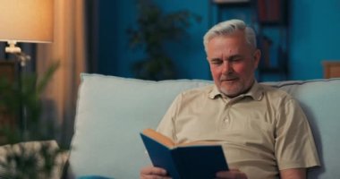 Kanepede oturan gülümseyen mutlu yaşlı adamın portresi. Yaşlı adam kameraya bakıyor.