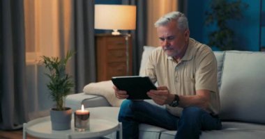 Oturma odasındaki kanepede oturan adam online alışveriş yapmaktan mutlu. Son sınıflar çok hoş.