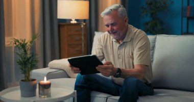 Oturma odasındaki kanepede oturan adam online alışveriş yapmaktan mutlu. Son sınıflar çok hoş.