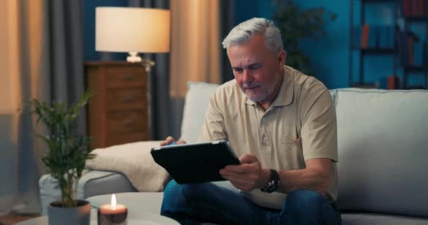 Mężczyzna siedzi na kanapie w salonie zadowolony z zakupów online. Starsi mężczyźni są zachwyceni. — Wideo stockowe