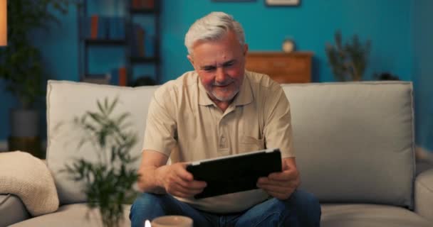 Мужчина зрелого возраста расслабляется вечером на диване в гостиной, работает — стоковое видео