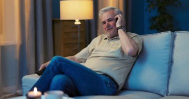 Emeklinin biri elinde uzaktan kumandayla TV 'nin önündeki koltukta dinleniyor.