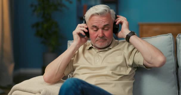 Un vieil homme se détend sur le canapé clique sur ses doigts sur le téléphone allumer un — Video