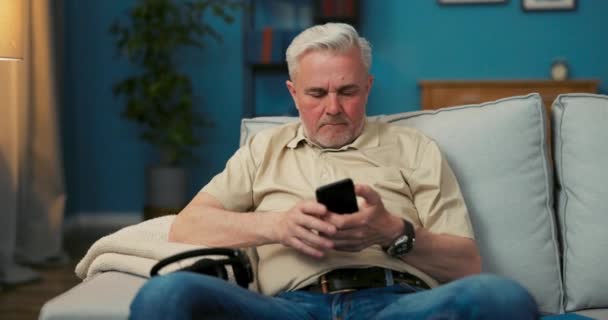 한 노인 이 소파에서 쉬면서 전화기를 켜고 손가락을 움직여 — 비디오