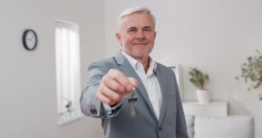 Kameraya doğru uzanan daire anahtarları, takım elbiseli, gri saçlı, olgun bir adam anahtarları verir, emlakçı, apartman sahibi, kullanacak yer verir.
