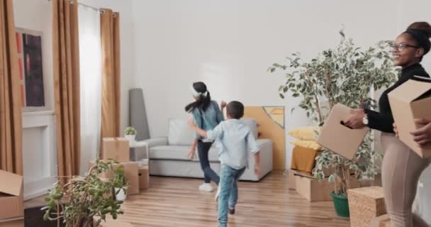 A szülők és a gyerekek belépnek az új lakásba, dobozokat hoznak, testvérek rohangálnak körbe-körbe a szobákban, mindenki mosolyog, boldog és izgatott a költözés miatt. — Stock videók
