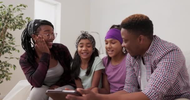 Mutlu bir aile, yenileme sırasında evdeki kanepede oturuyor. Evli bir çift ve iki kızı oda renkleri için tablet okuyor. Babaları, annelerinin şok olduğunu söylüyor. — Stok video