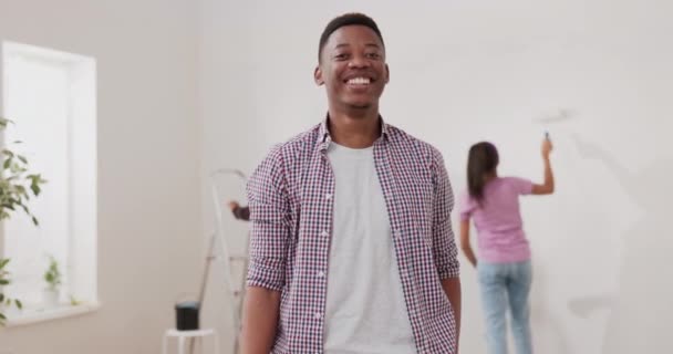 Un hombre sonriente con una camisa a cuadros está renovando un apartamento con su esposa y — Vídeos de Stock