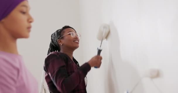 Dulce chica está pintando la pared con un rodillo que está cubierto de pintura blanca juntos — Vídeos de Stock