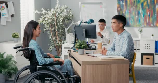 Mujer está sentada en silla de ruedas en el escritorio en la oficina, frente a su empleador se sostiene — Vídeos de Stock