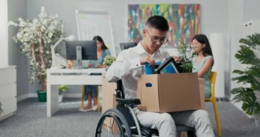 Gözlüklü genç bir ofis çalışanı yaralanmış, sakat, tekerlekli sandalyede elinde bir kutu