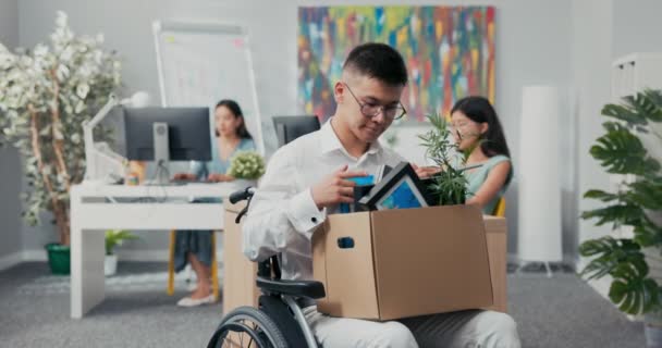 Молодий працівник корпоративного офісу поранений, нещасний випадок, інвалід, у інвалідному візку, тримає коробку атрибуції від — стокове відео