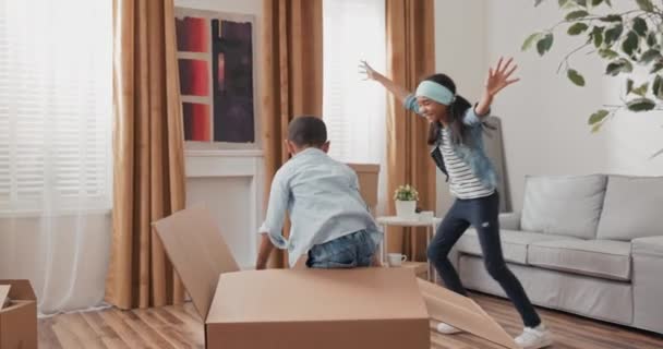 Een meisje spelen verstoppertje met haar broer opent een verhuizing doos van waaruit — Stockvideo