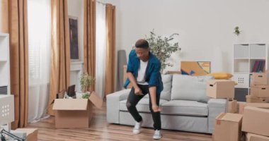 Mutlulukla dolu yakışıklı adam yeni dairede dans ediyor. Taşınıyor, karton kutular taşıyor.