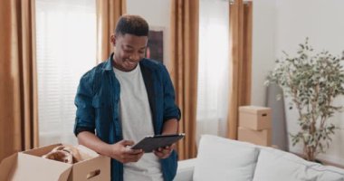 Genç bir çocuk yeni dairesinde takılıyor. Karton kutuları açıyor.