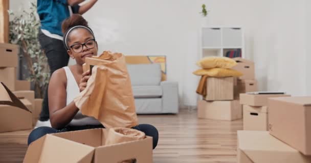 Małżeństwo wprowadza się do nowego mieszkania kobieta siedzi na podłodze rozpakowywania kartonowych pudełek — Wideo stockowe