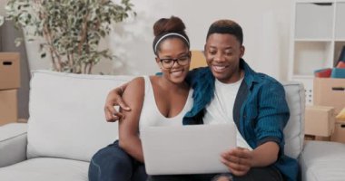 Bir adam kanepede dinlenirken kadınını kucaklıyor, dizüstü bilgisayar tutuyor.