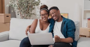 Bir adam kanepede dinlenirken kadınını kucaklıyor, dizüstü bilgisayar tutuyor.