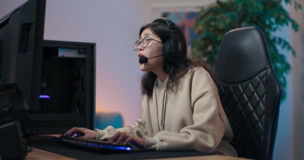 Woman loses computer game looking disappointed at monitor, covers face with hands shakes head negatively. Girl in headset spends time in room lit by led lights — ストック動画