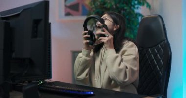 Genç Asyalı kız ekranda bilgisayar başında oturuyor, kadın kulaklığı takıyor, takım üyeleriyle konuşuyor, online aksiyon oyunları oynamaya başlıyor.