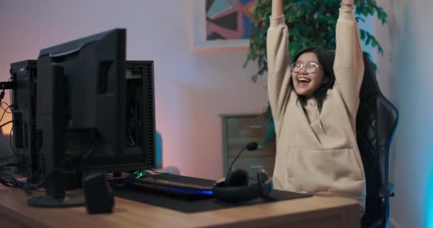 Дівчина грає в ігри на комп'ютері. Про-гравець виграє чемпіонат Інтернету, жінка піднімає руки в повітря заради радості, обертається на поворотному кріслі крики з щастям, кладе навушники слухає музику співає — стокове відео