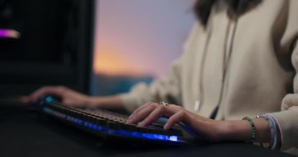 Close-up on hands of woman playing on professional color backlit keyboard, led lighting, transition to focused face of girl in headset gamer talking to team members and passing game level — Vídeo de stock