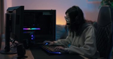 Odaklanmış kadın geceleri bilgisayar oynar, oda lambayla aydınlatılır, kız oyuncu parmaklarını güçlü bir şekilde klavye tuşlarına vurur, vücut hareketleri yapar oyunu hisseder, genç kız sanal dünyada yaşar.