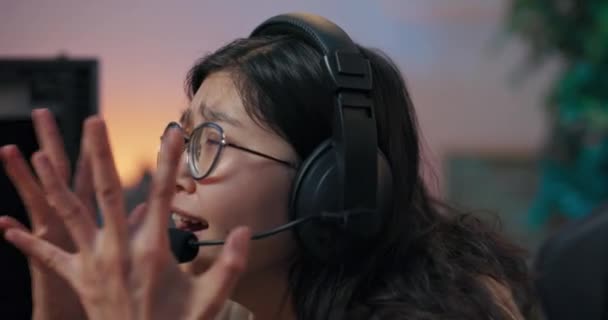 Лицо женщины в очках и гарнитуре, расстроенной из-за проигрыша компьютерной игры, ломается, руки закрывают лицо криками, плачем, печалью от поражения в виртуальной реальности. — стоковое видео