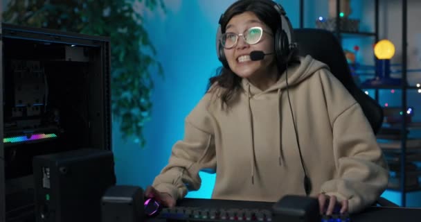 Glückliches Mädchen in Sweatshirt und Brille mit Kopfhörern spielt Online-Videospiele mit Freunden, spricht mit ihnen über Mikrofon, Pass-Levels, Runden, Strategie, Sieg, Freude schreit Sieg — Stockvideo