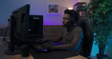 Hayal kırıklığına uğramış kızgın oyuncu oyunu kaybeder, elleri birbirine kenetlenmiş yüz, kulaklık takar, ne yazık ki monitöre bakar, mavi ve mor ışıklı oda