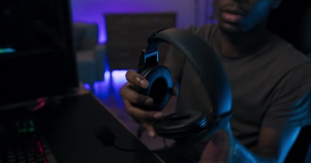 Close-up on a headset which is taken by man playing computer games on professional color backlit keyboard, the guy is putting on headphones to talk friends led lighting — Stock Video