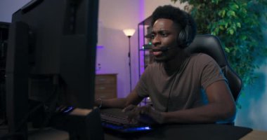 Bir adam bilgisayarda tetikçiyi oynuyor. Takım arkadaşıyla kulaklıkla konuşuyor. Adam yuvarlak bir bakış atıyor.