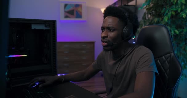 Профессиональный видео-геймер афроамериканец мужчина ориентирован на победу в раунде имеет наушники переговоры с соперниками, не проходит уровень покрывает лицо рукой выпускает воздух вздыхает в гневе, неудача в Интернете — стоковое видео
