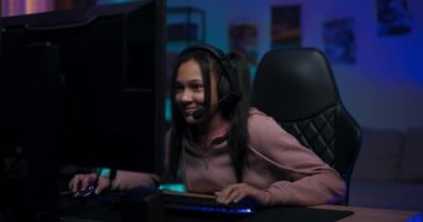 Profesyonel oyuncu genç kız kulaklıkla takımla bilgisayar oyunu oynuyor, sanal şampiyonada turu kazanıyor, seviyeyi geçiyor, kadın zaferden zevk alarak elini kaldırıyor.