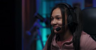 Odaklanmış genç kız video oyunlarına tutkulu, konsantrasyon içinde bilgisayarda oynuyor bir sonraki seviyeye geçiyor, yuvarlak, kulaklığı var, odada mor ışıklar var.