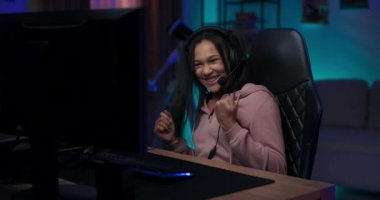 Profesyonel bir oyuncu, hayranları için sosyal medyadan canlı yayın yapıyor. Bir sonraki seviyeye geçmeye odaklanmış bir kulaklıkla takımla konuşuyor. Oda mavi ve mor ışıklarla aydınlanıyor.