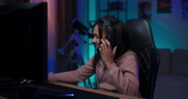 Profesyonel bir genç oyuncu, mavi ve mor LED 'ler tarafından yakılan bir odada çevrimiçi e-spor şampiyonası için hazırlanıyor, bir kulaklık takıyor, bir klavye ve oyun oynamak için bir fare kaçırıyor.