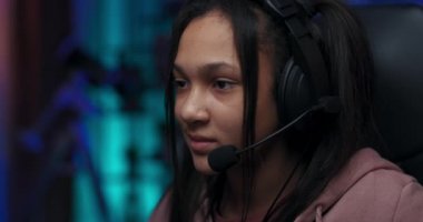 Gülümseyen genç bir oyuncunun yakın plan portresi, kız oyunu kazanmaktan mutlu, seviyeyi geçiyor, gencin kulaklığı var, profesyonel oyun aksesuarları, mavi ışıklarla aydınlatılmış oda.