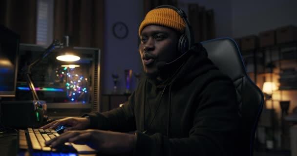 Mens δωμάτιο τη νύχτα φωτίζεται από φώτα LED. Ένας επαγγελματίας παίκτης κάθεται μπροστά από έναν υπολογιστή παίζοντας online παιχνίδια στο διαδίκτυο με μια ομάδα hes μιλάμε μέσα από ένα headset.Relaxed τύπος κοιτάζοντας κάμερα γελώντας — Αρχείο Βίντεο