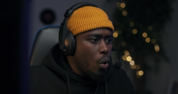 Shocked man, professional computer gamer, looks at computer screen, talks to team through headset, upset from loss removes headset. Dark room lit by led lights — Stock Video