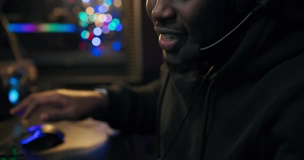 Una habitación oscura iluminada por luces led, un hombre con cuero negro se sienta frente a una computadora por la noche hablando a través de un auricular a los miembros del equipo frotándose las manos antes de la siguiente ronda — Vídeo de stock