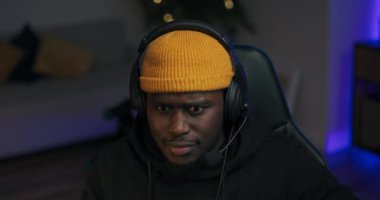 Kapüşonlu ve şapkalı bir çocuk karanlık bir odada bilgisayarın önünde oturuyor. Adamın bir kulaklığı var. Evinden uzaktan çalışan ekip üyeleriyle, iş arkadaşlarıyla konuşuyor.