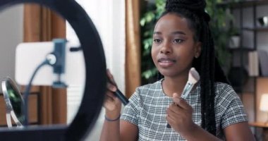 At kuyruğu örgülü koyu tenli bir kadın doğru makyaj fırçalarını nasıl seçeceğine dair kısa talimat videoları kaydetti. Kız sosyal medyada güzellik içeriği yaratıyor.