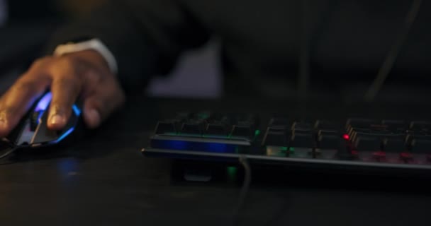 Koyu tenli bir adamın profesyonel bir arka aydınlatma klavyesinde çalan eli yakın plan, o bir bilgisayarda kurşun bir fare kullanıyor. — Stok video