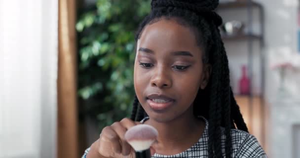 Nahaufnahme des Gesichts einer Frau mit dunkler Haut afroamerikanischer Abstammung. Die Visagistin spricht mit einem Freund, dem sie kosmetische Ratschläge gibt, und beschreibt die Foundation Pinsel, die sie verwendet — Stockvideo