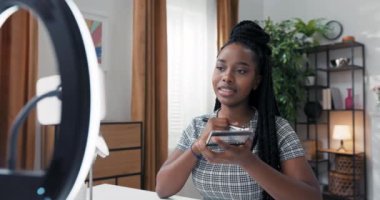 Yüze bronzlaştırıcı sürme talimatları. Rastalı bir kadın sosyal medyada canlı yayın yapıyor. Yüzük ışığı kullanan kız internette güzellik tavsiyeleri veriyor.