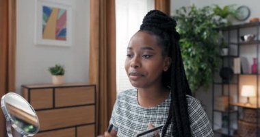 Bir kız, halka ışığı ve telefon tripodu kullanarak video çekiyor. Bir makyaj sanatçısı, yanaklarına fosforlu kalem sürmek için fırça kullanarak, yüzü düzgünce nasıl vurgulayacağını öğretir.